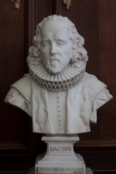 Marble bust of Francis Bacon wearing a ruff and formal jacket. Pictured against a wood-panelled wall. 