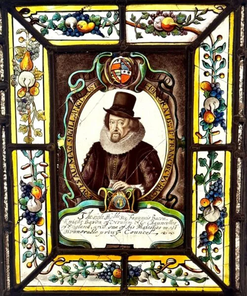 A very decorative image in stained glass with Francis Bacon at its centre surrounded by a vine-like plants with fruit. There is an inscription in English below and coat of arms above his head. 