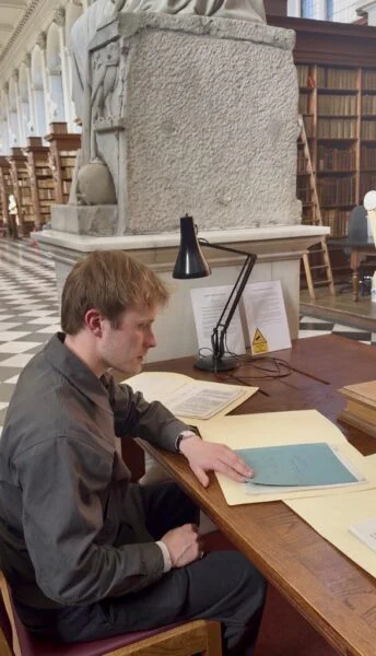 young man at a desk in a library looking at documents