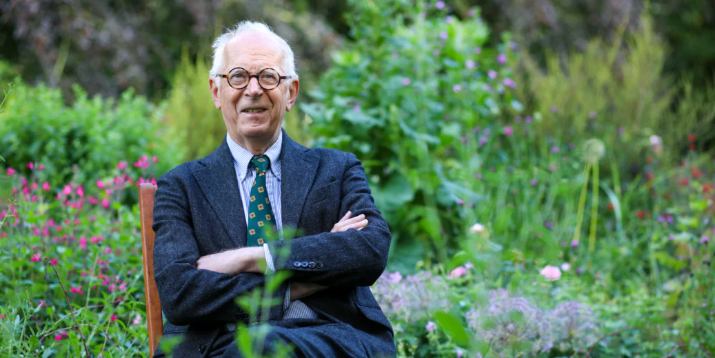 A man in a blue suit sitting on a chair in a garden.