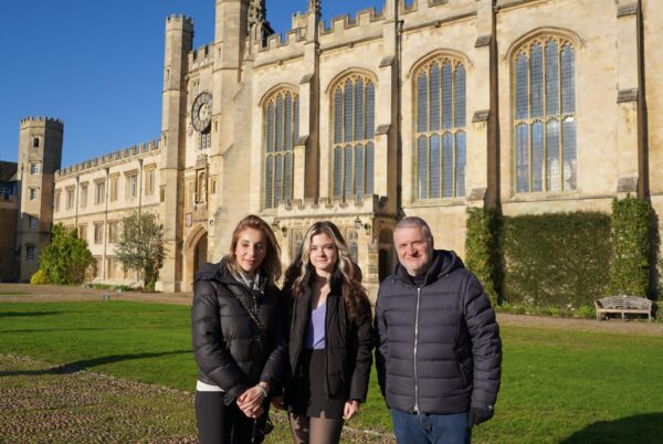 Two women and a man with Trinity College Chapel and Clock Tower behind them. 