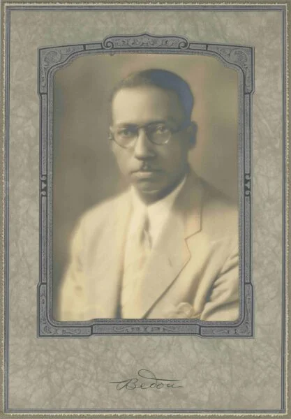 Black man in a pale suit and tie in a black and white portrait studio image. 