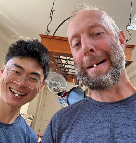 Two men smiling with small tablets in their mouths. 